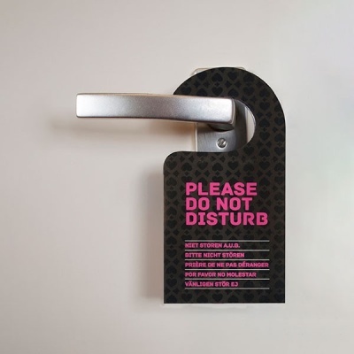 Sinal de porta preto com texto rosa 'PLEASE DO NOT DISTURB' na maçaneta.