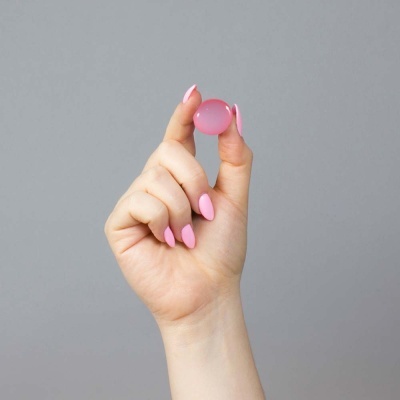Mão feminina a segurar pequena esfera cor-de-rosa translúcida sobre fundo cinza