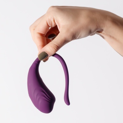 Dispositivo sexual de silicone roxo sendo segurado por uma mão com unha pintada verde