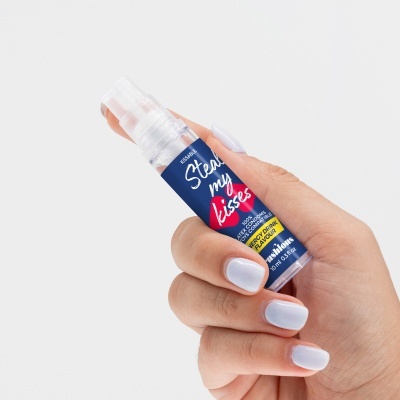 Frasco pequeno de spray com rótulo azul segurado por mão feminina com unhas brancas