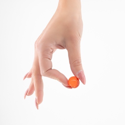 Mão feminina segurando cápsula laranja transparente