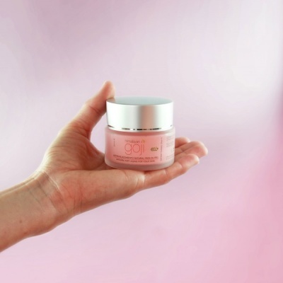 Frasco de creme para cuidados da pele cor de rosa com tampa prateada numa mão