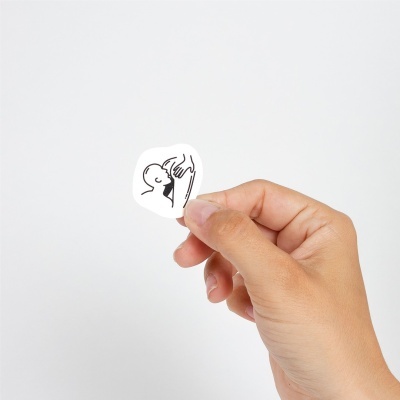 Etiqueta pequena branca com desenho a preto de silhuetas humanas, segurada por mão sobre fundo branco