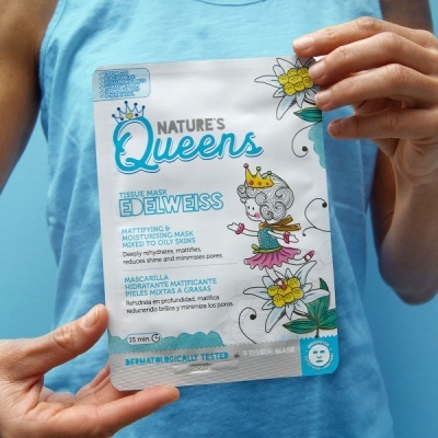 Máscara facial Nature's Queens com embalagem azul e branca, segurada por pessoa com t-shirt azul.