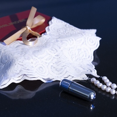 Conjunto de lingerie branca rendada, caixa vermelha com fita dourada, colar de pérolas com pendente metálico prateado