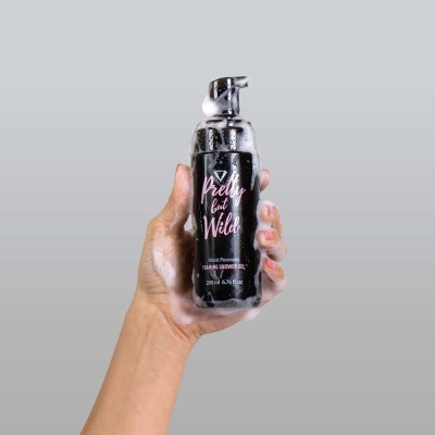 Frasco de gel de duche preto com doseador e espuma numa mão