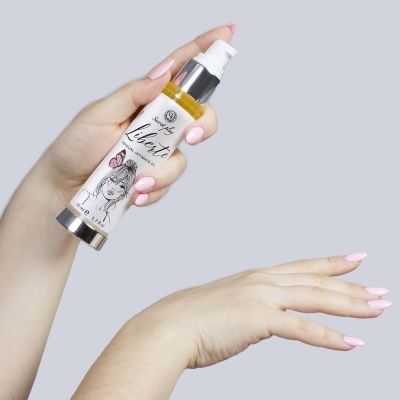 Frasco de creme com rótulo ilustrado sendo segurado por mão com unhas cor rosa, aplicado na outra mão