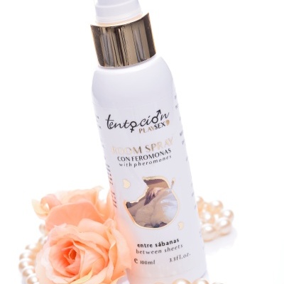 Frasco de room spray branco com detalhes dourados rodeado por colar de pérolas e rosas cor de rosa