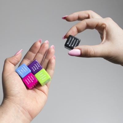 Mãos segurando quatro marcadores de cores e um marcador preto com texto.