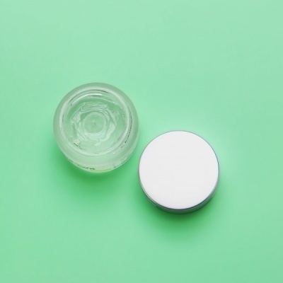 Frasco de vidro transparente com tampa branca ao lado sobre fundo verde claro