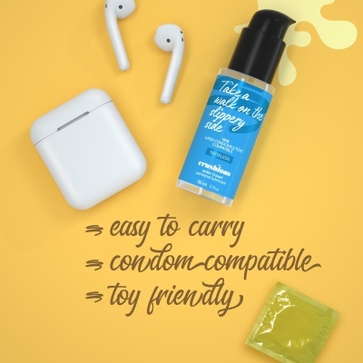 Frasco azul de lubrificante íntimo Crownshop com auriculares e preservativo sobre fundo amarelo