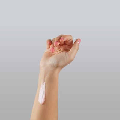 Braço com creme aplicado no antebraço em fundo cinza claro