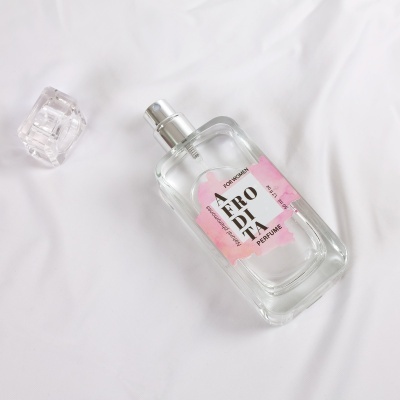 Frasco de perfume transparente com etiqueta rosa e texto AFRODITA