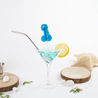 cocktail azul em copo de martini com rodela de limão e agitador azul, rodeado por seixos e madeira