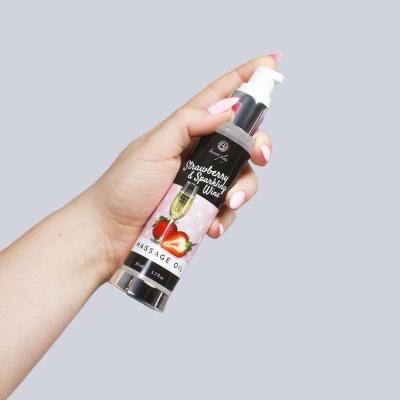 Frasco de óleo de massagem com morangos e champanhe numa mão