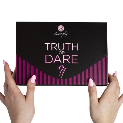 Caixa preta do jogo Truth or Dare com detalhes roxos, segurada por mãos com unhas rosa claro