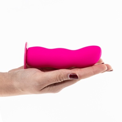 Vibrador rosa de silicone suportado na mão com unhas pintadas