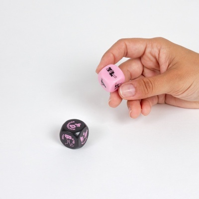 Dados de jogo em plástico, rosa e preto com símbolos, numa superfície branca.