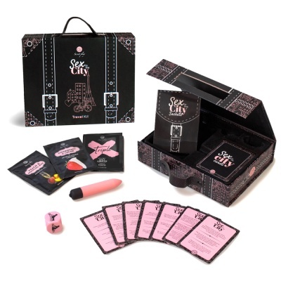 Kit de viagem Sex and the City com cartas, dados, vibrador e embalagem em formato de mala preta.