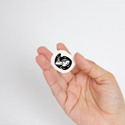 Mão a segurar um autocolante redondo branco com desenho preto