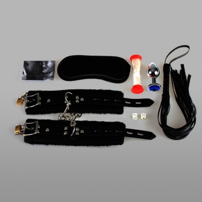 Conjunto BDSM com algemas pretas, venda, flogger, plug metálico e dados.