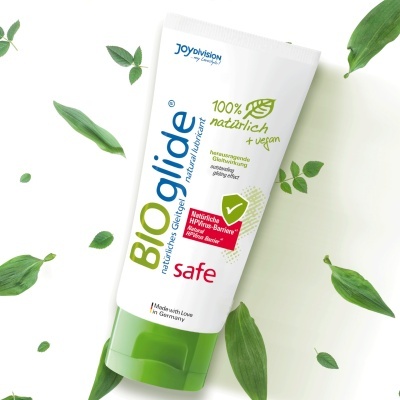 Tubo de gel lubrificante BIOglide com design branco e verde, rodeado por folhas verdes
