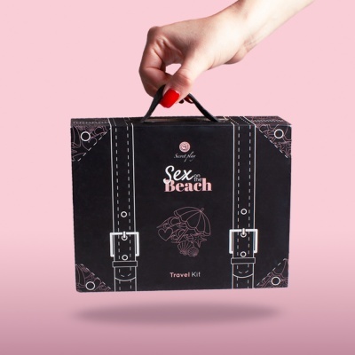 Mala de viagem preta com texto e ilustrações segurada por mão feminina sobre fundo rosa