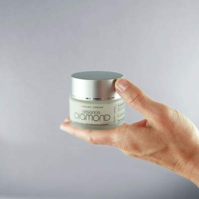 Frasco pequeno de creme Essent Diamond com tampa prateada numa mão.