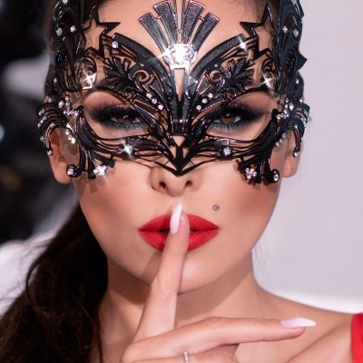 Máscara facial preta decorativa com estrelas usada por mulher com batom vermelho e unhas brancas.