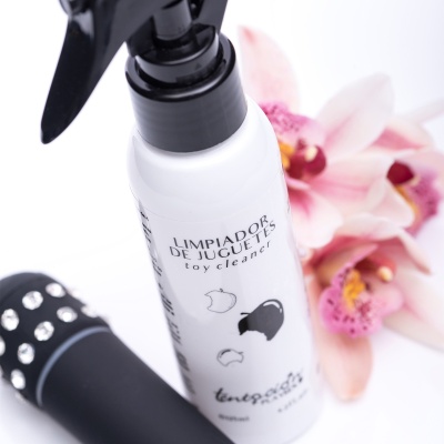 Frasco branco com pulverizador preto do Limpiador de Juguetes ao lado de objeto preto com detalhes prateados e flores rosas