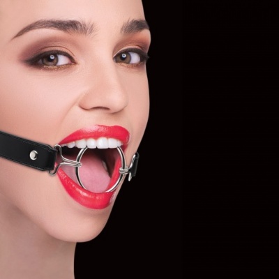 Mulher com mordaça de metal circular e correia preta num fundo preto