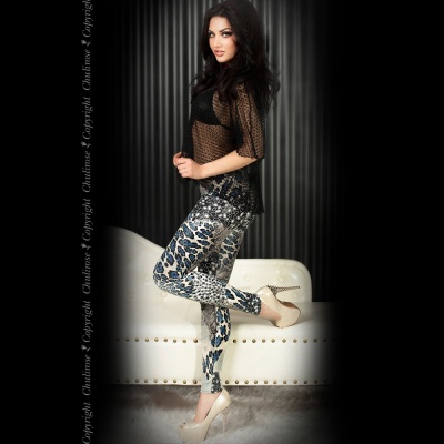 Modelo veste calças animal print azul e blusa preta transparente junto a sofá branco.