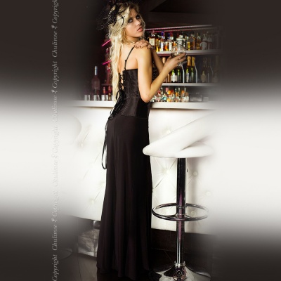 Mulher em vestido preto longo ao lado de balcão branco com banquetas altas em bar