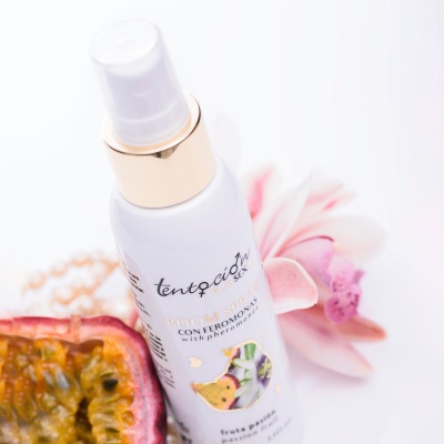 frasco branco de spray com tampa transparente e detalhes dourados junto a maracujá cortado e flor cor-de-rosa