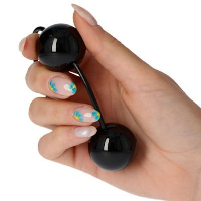 Mão com unhas decoradas segura bolas sexuais pretas ligadas