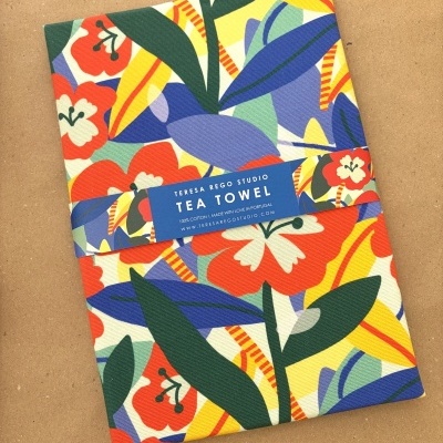 Pano de chá colorido com padrão floral e etiqueta azul sobre fundo castanho