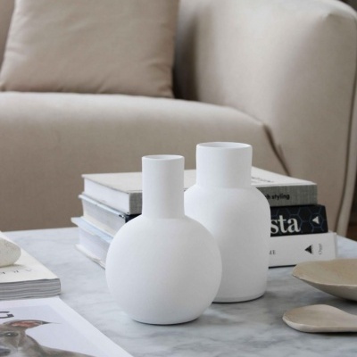 Mesa de mármore com vasos brancos e livros em frente a sofá bege