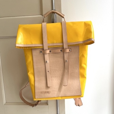 Mochila amarela com detalhes castanho claro e alças, pendurada numa porta