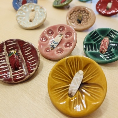 Botões coloridos de cerâmica com padrões e tecido no furo central em superfície clara.