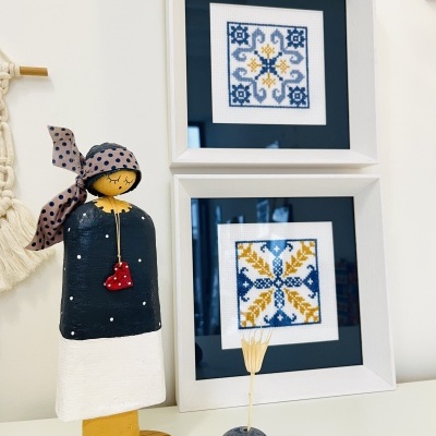 Dois quadros brancos com bordados e figura decorativa de madeira em fundo branco