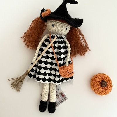Boneca de croché com vestido preto e branco, chapéu de bruxa, bolsa laranja e vassoura com abóbora de croché