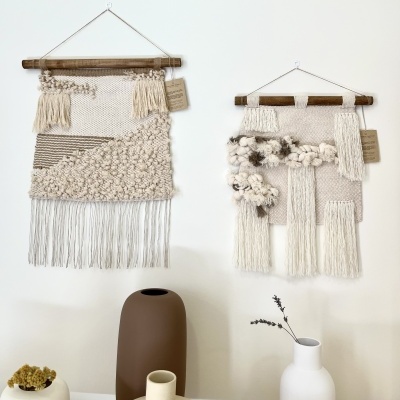 Dois tapetes decorativos de parede em tons neutros pendurados e três vasos cerâmicos com ramos secos