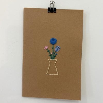 Cartaz castanho com bordado de vaso e flores coloridas