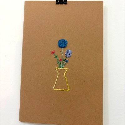 Caderno castanho com bordado de vaso amarelo com flores coloridas