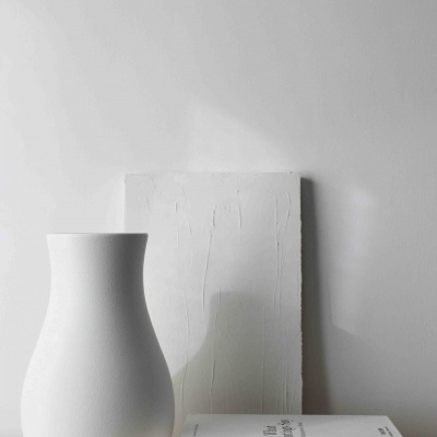 Vaso branco de cerâmica junto a livro 'What Paintings Say' e tela branca sobre superfície de madeira.