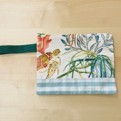 Bolsa pequena estampada com tartarugas e plantas, com base azul quadriculada e alça verde