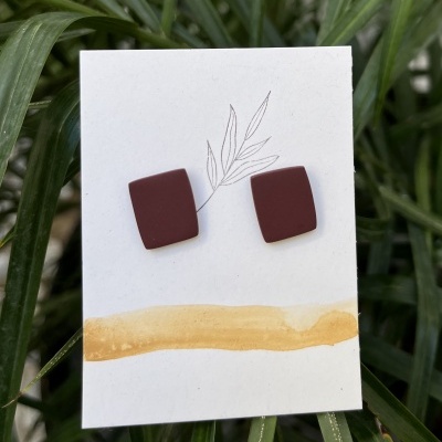 Brincos castanhos quadrados exibidos num cartão decorado