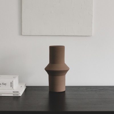 Vaso cerâmico castanho geométrico sobre mesa preta com livros e tela branca na parede
