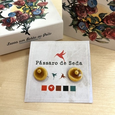 Brincos amarelos com pérolas em cartão de apresentação e caixas decoradas com ilustração floral.
