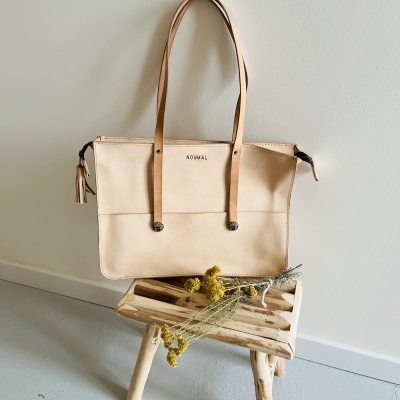 Mala de mão bege com alças castanhas pendurada na parede acima de banco de madeira com flores secas amarelas